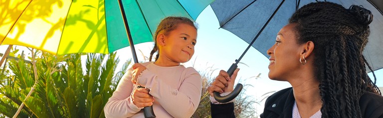 A mom and daughter talk with each other under colorful umbrellas